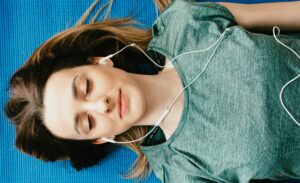 Frau liegt auf Sportmatte und hört Musik über Kopfhörer